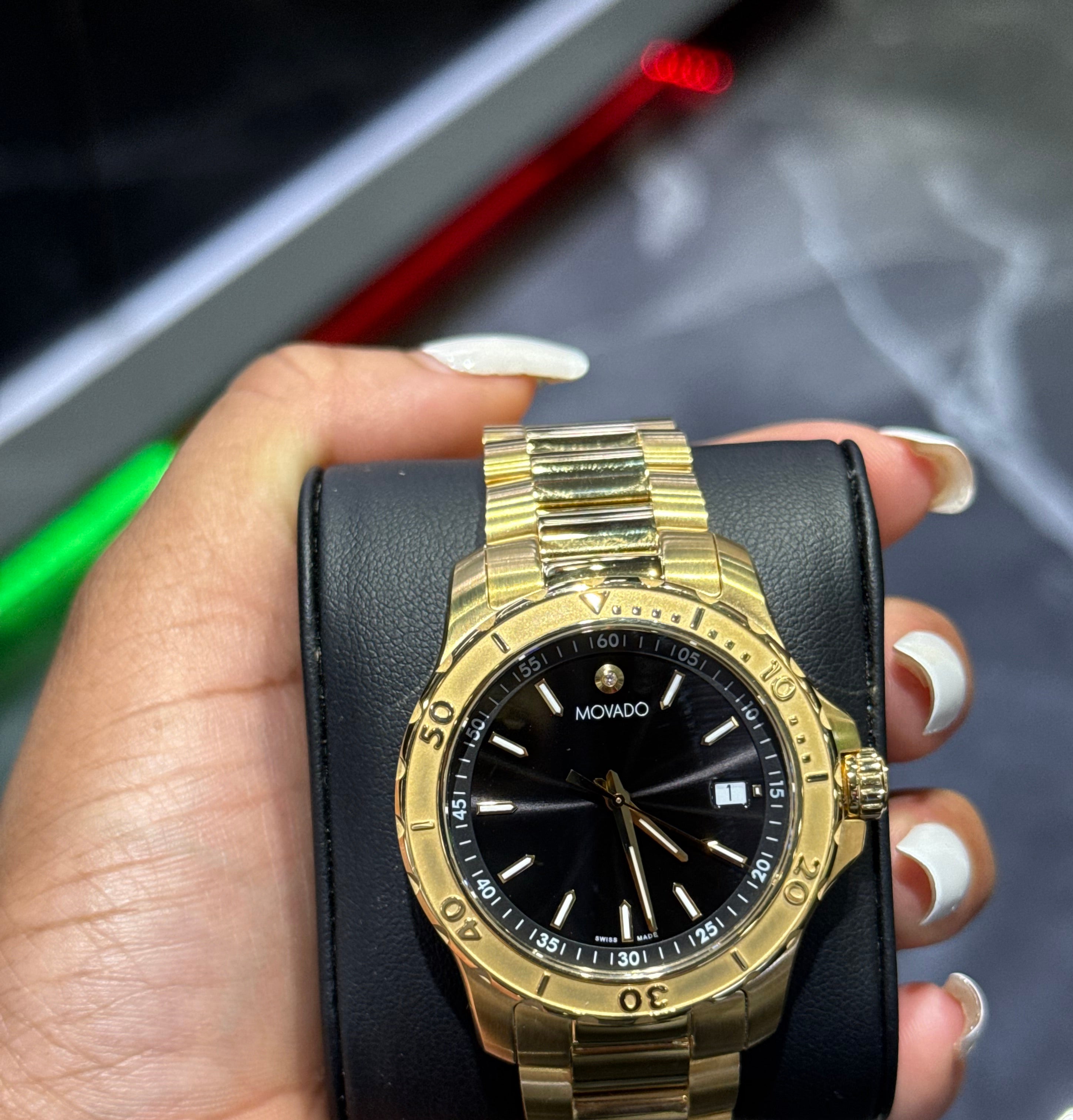 Gold wristwatch with black face held in a hand against a blurred background