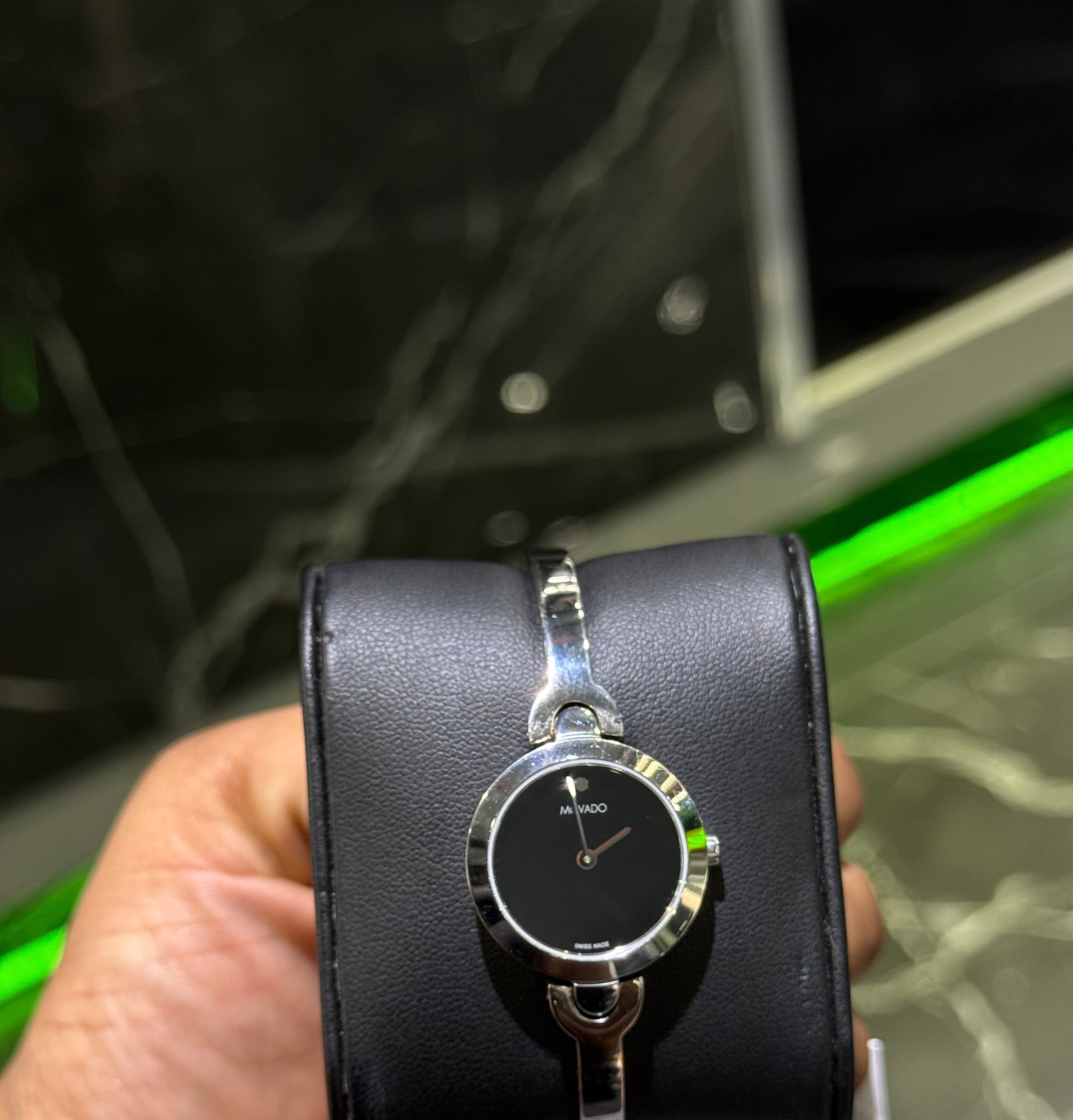 Black wristwatch with silver band held by a hand against a blurred background