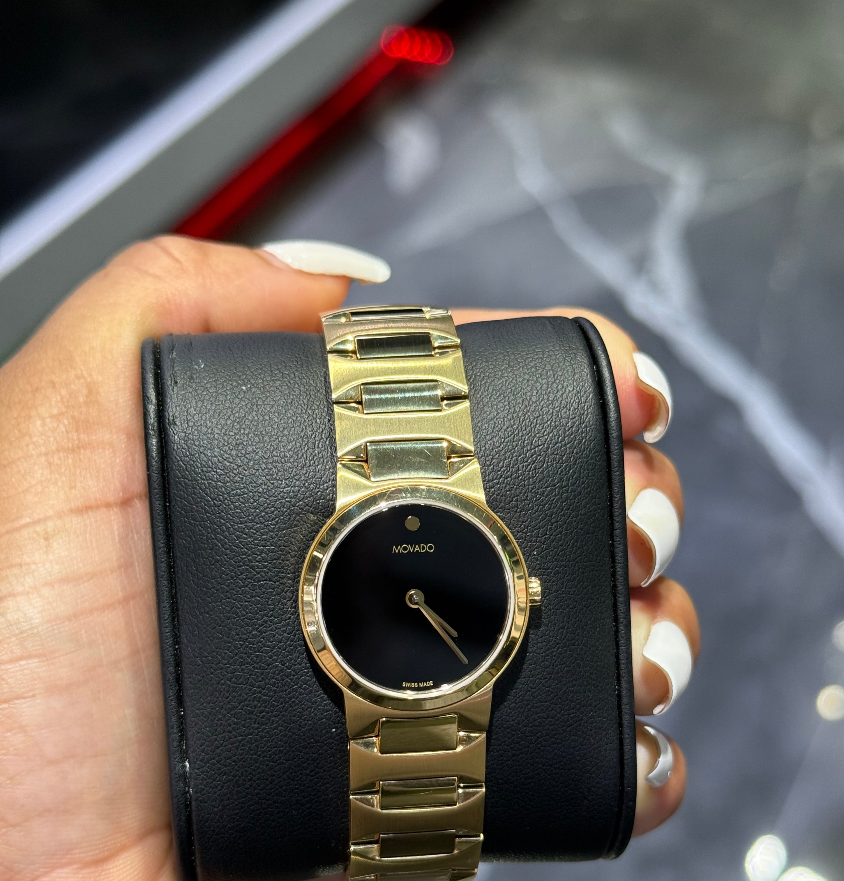 Gold wristwatch with black face held in a hand against a blurred background