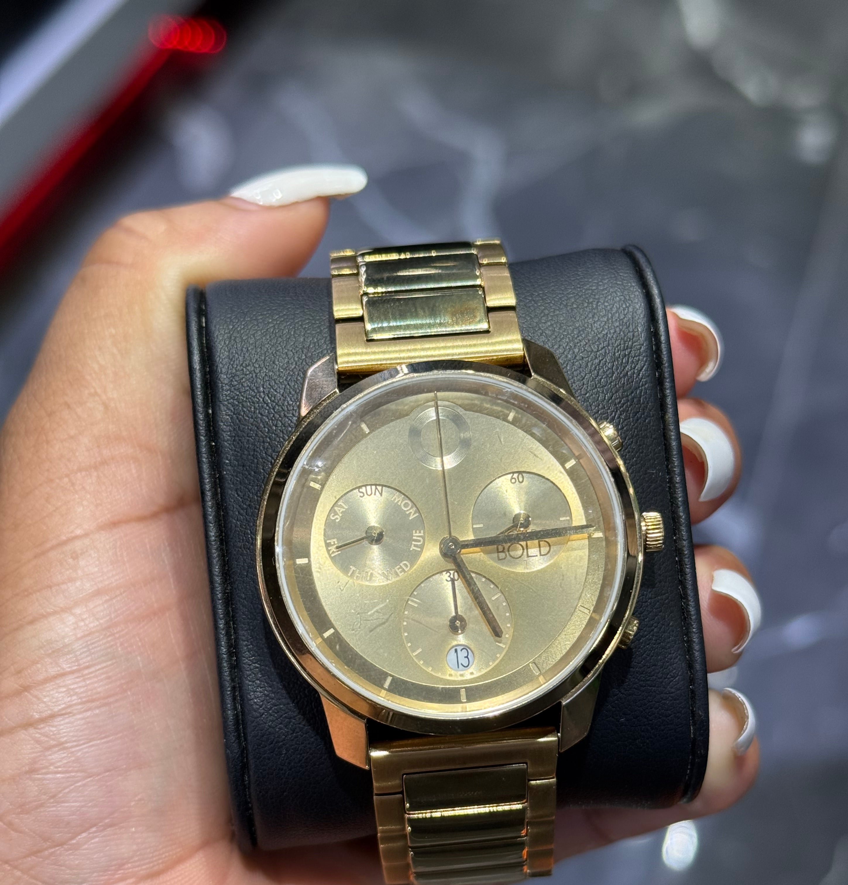 Gold watch with black leather strap held in a hand against a blurred background