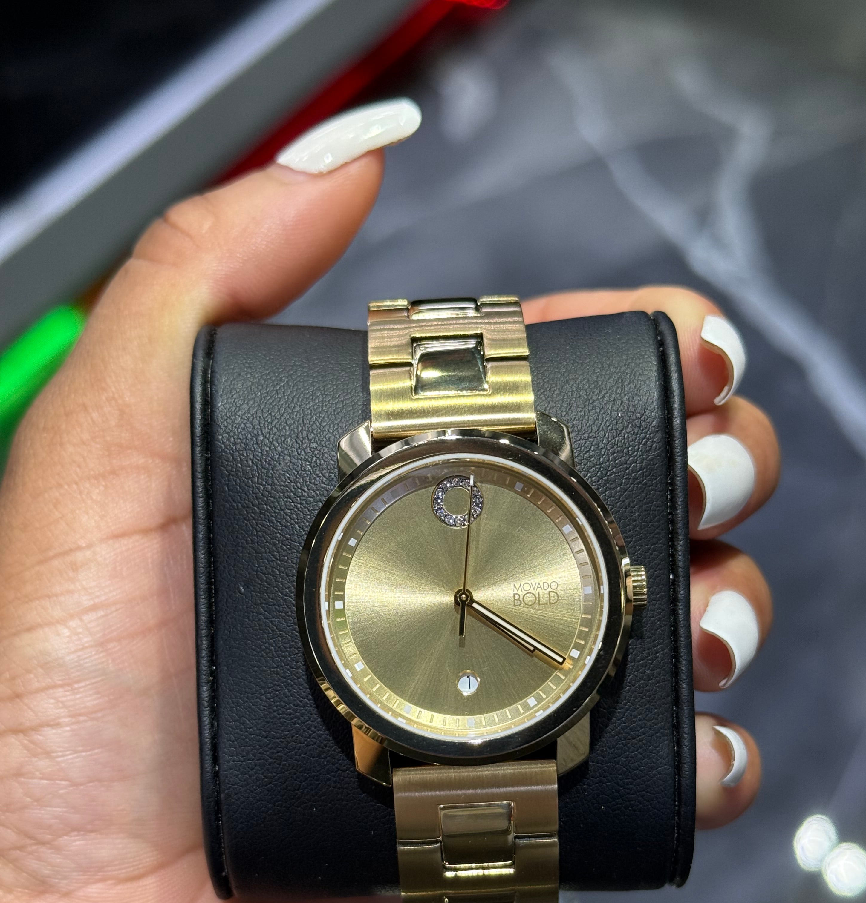 Gold watch with black leather strap held by a hand against a blurred background