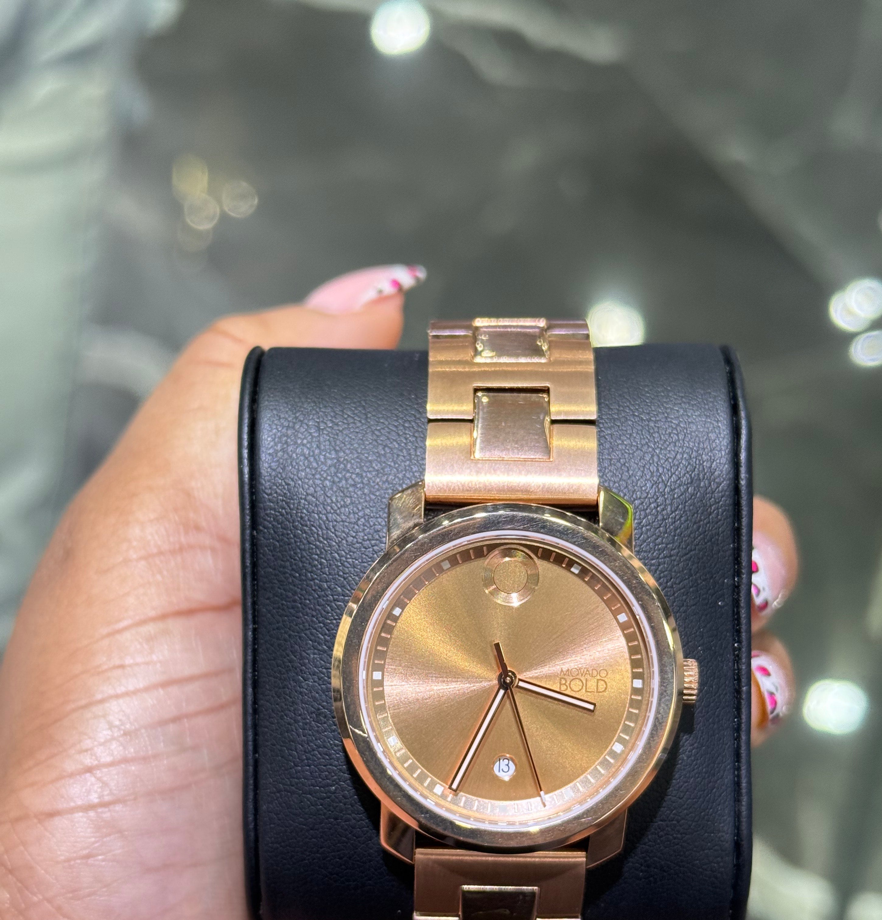 Gold watch with black leather strap held by a hand against a reflective surface.