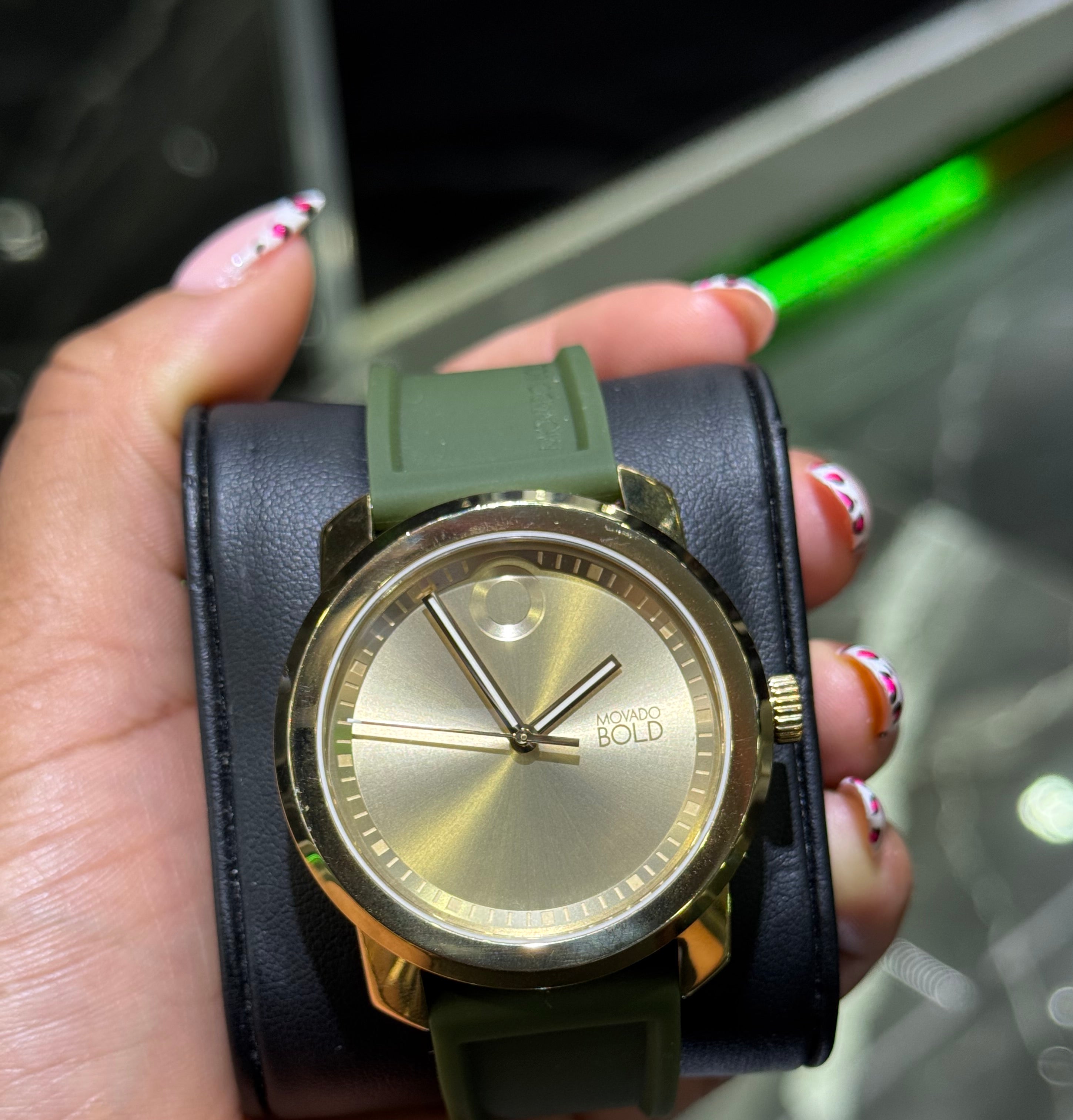 Gold watch with black strap held in a hand against a blurred background