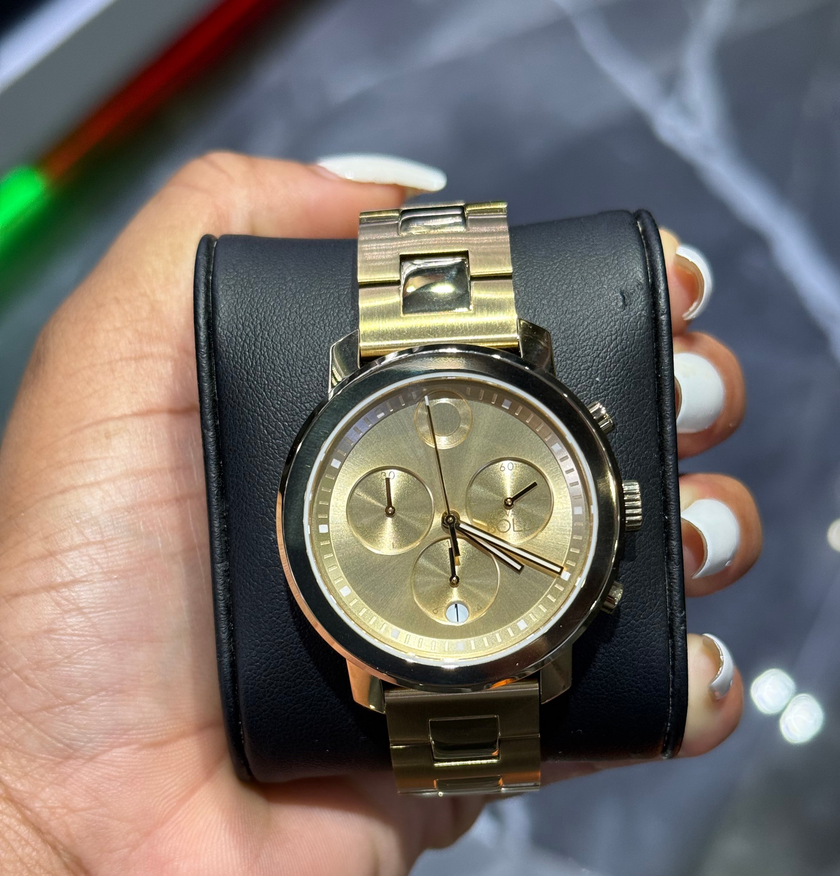 Gold wristwatch with black leather strap held in a hand against a reflective surface.