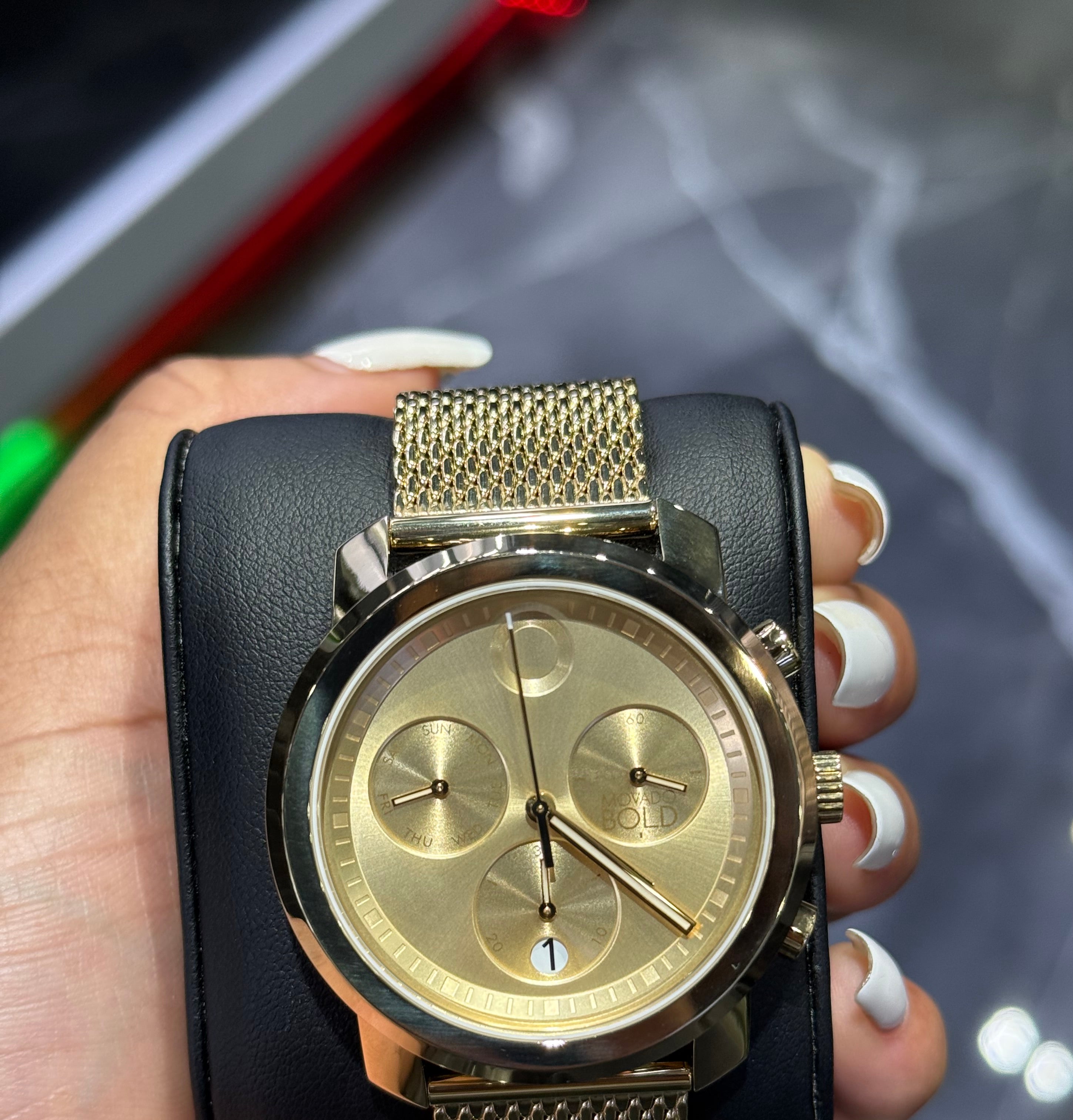 Gold watch with black strap held in a hand against a blurred background