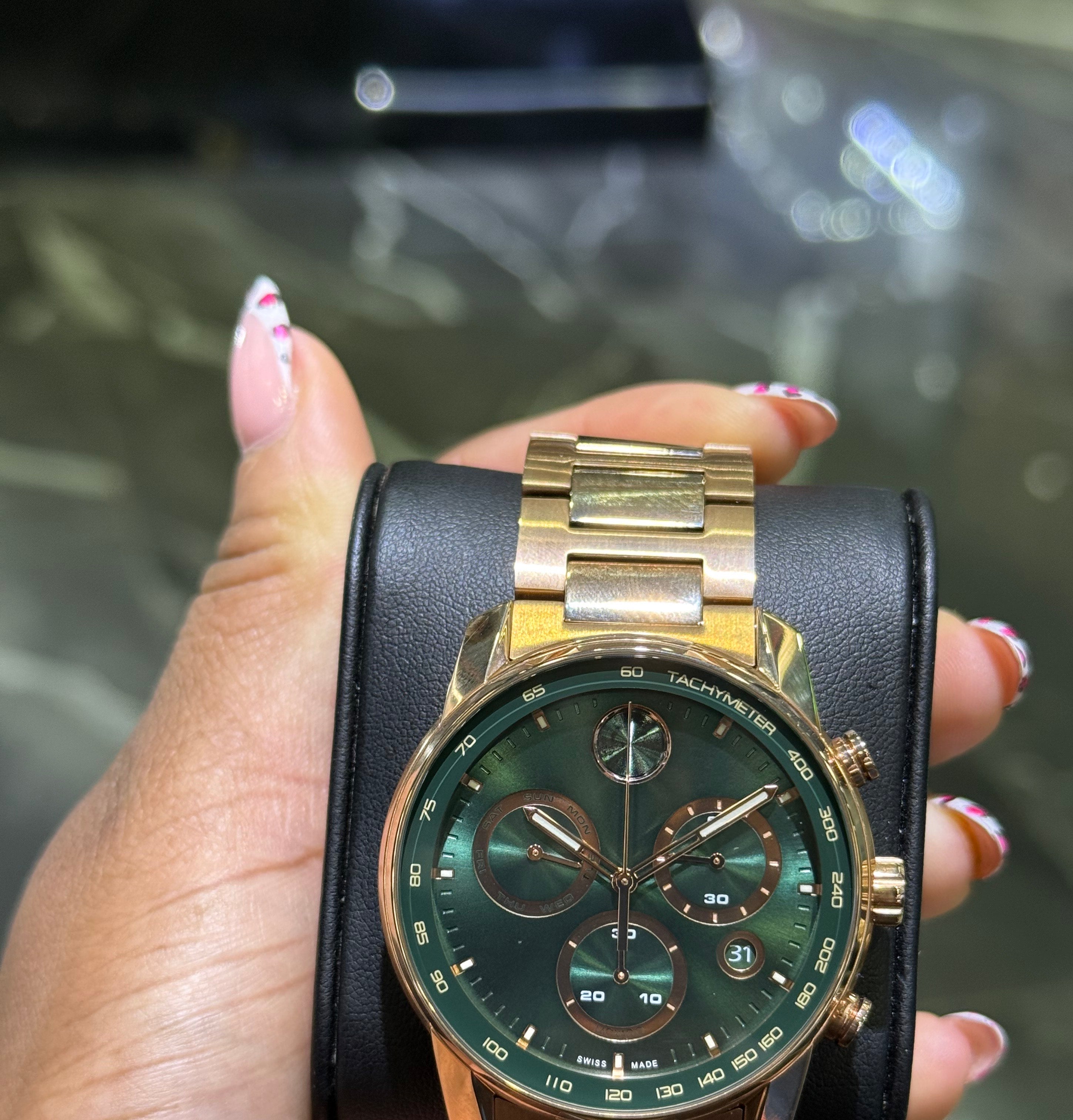 Gold and black wristwatch held by a hand with a blurred background