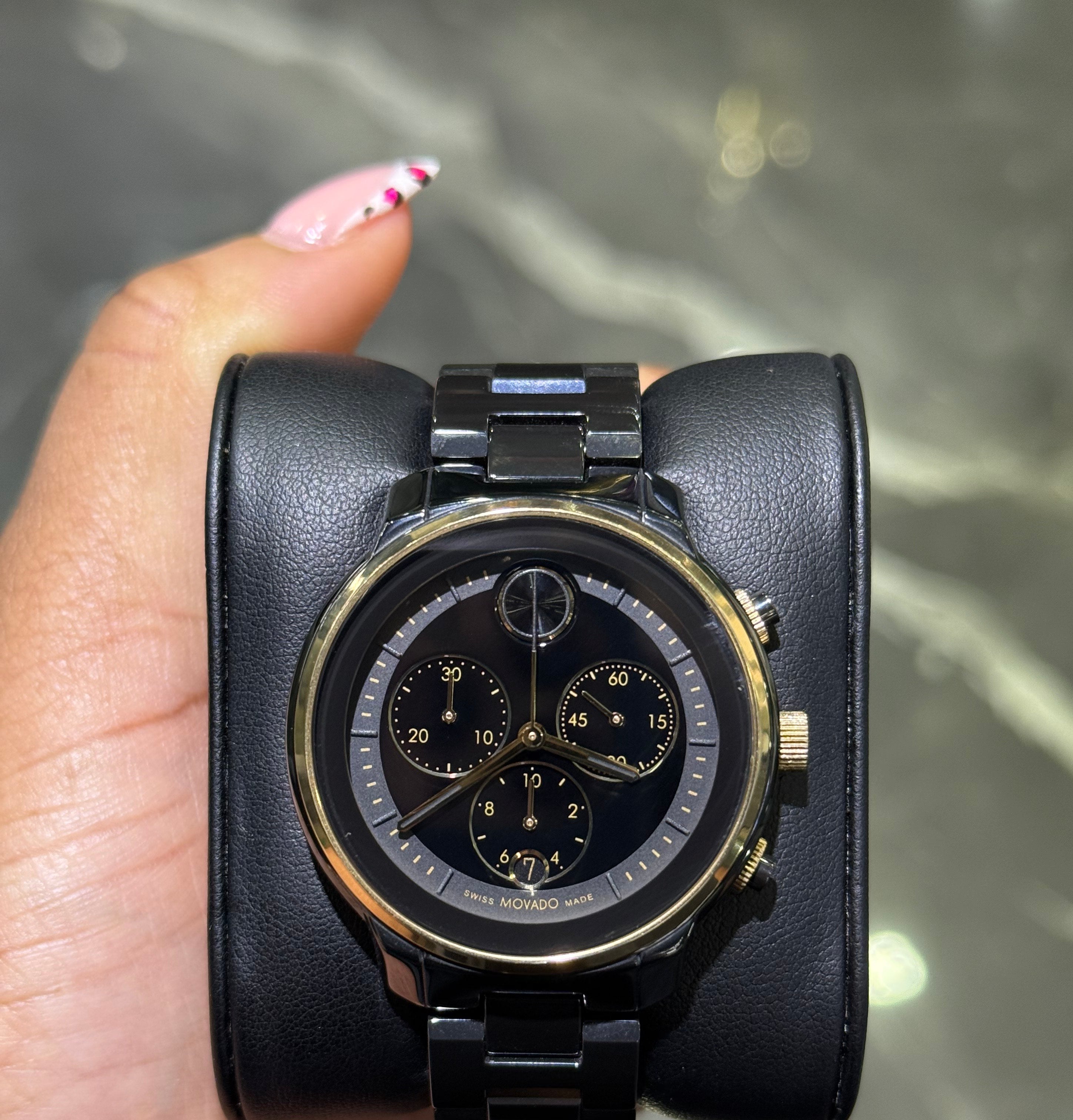 Black wristwatch with gold accents held in a hand against a neutral background