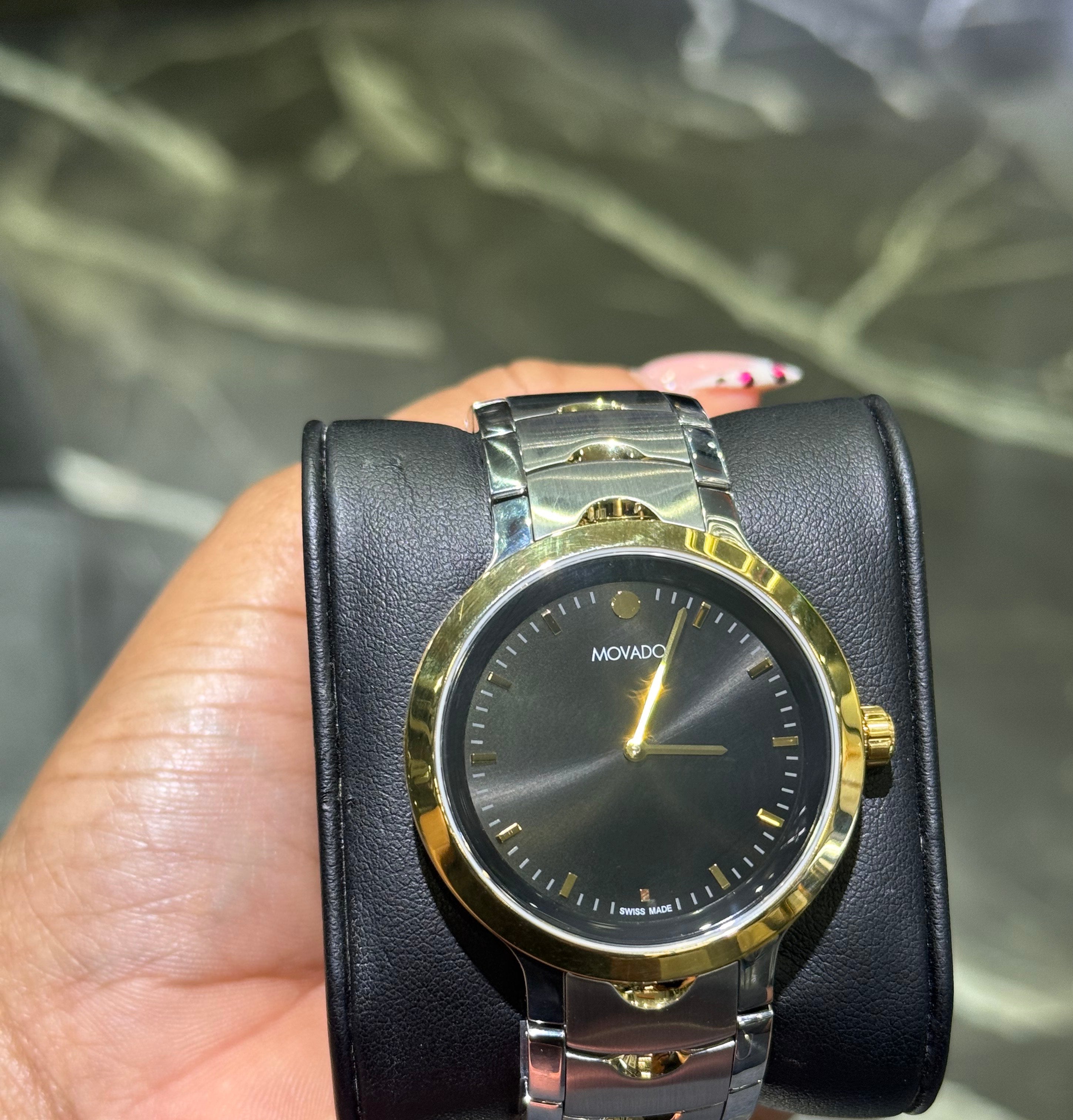 Gold and black watch held in a hand with a blurred background