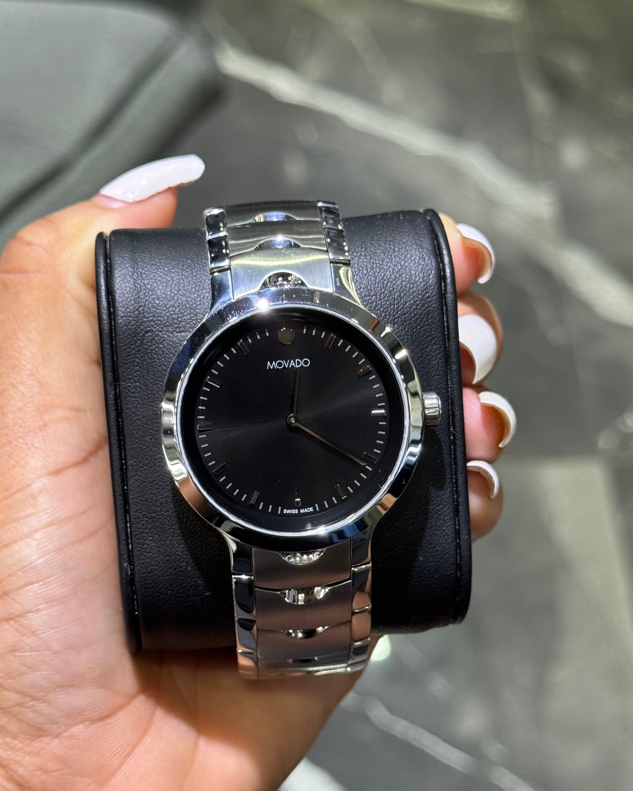 Hand holding a silver watch with a black face against a blurred background