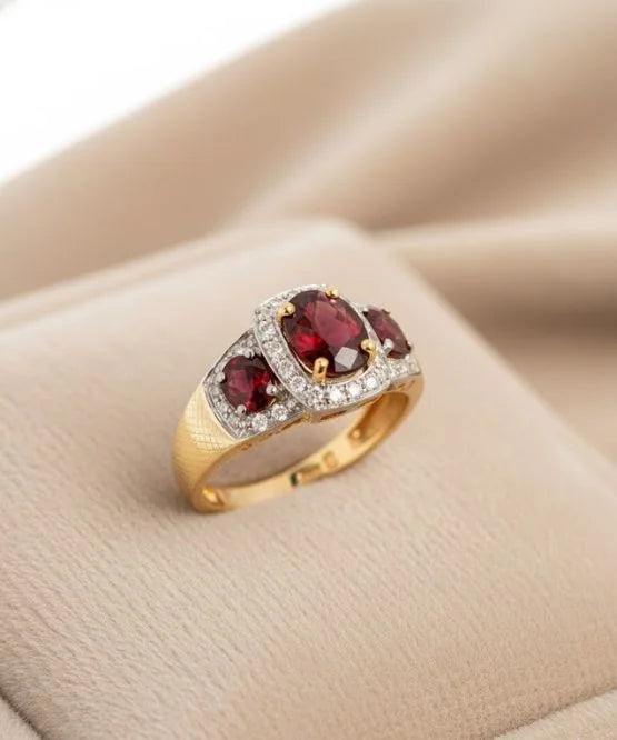 Gold ring with red gemstones on a beige surface