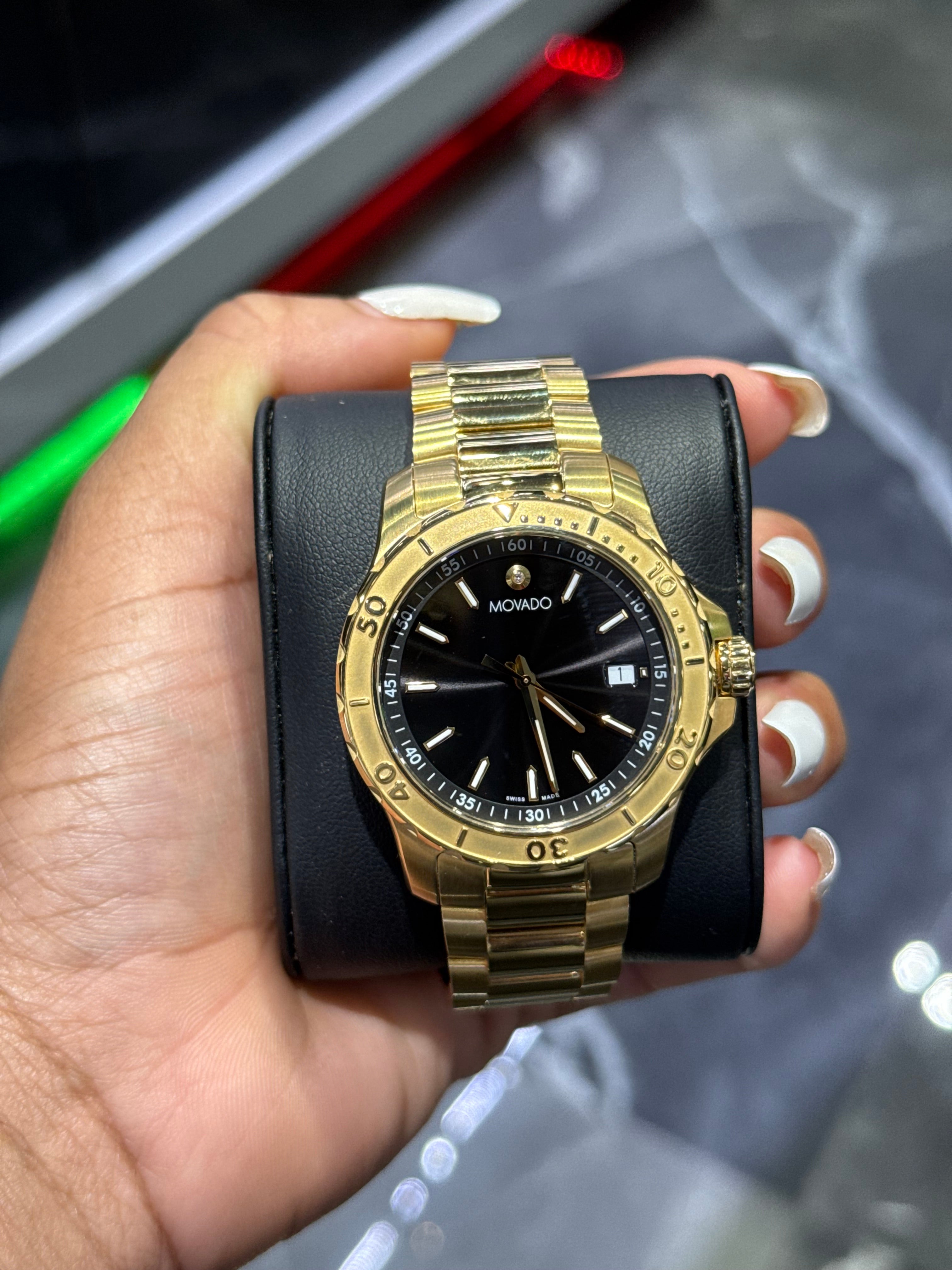 Gold wristwatch with black face held in a hand against a blurred background