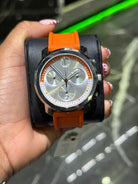 Hand holding a watch with an orange strap against a blurred background