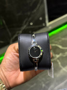 Black wristwatch with silver band held by a hand against a blurred background