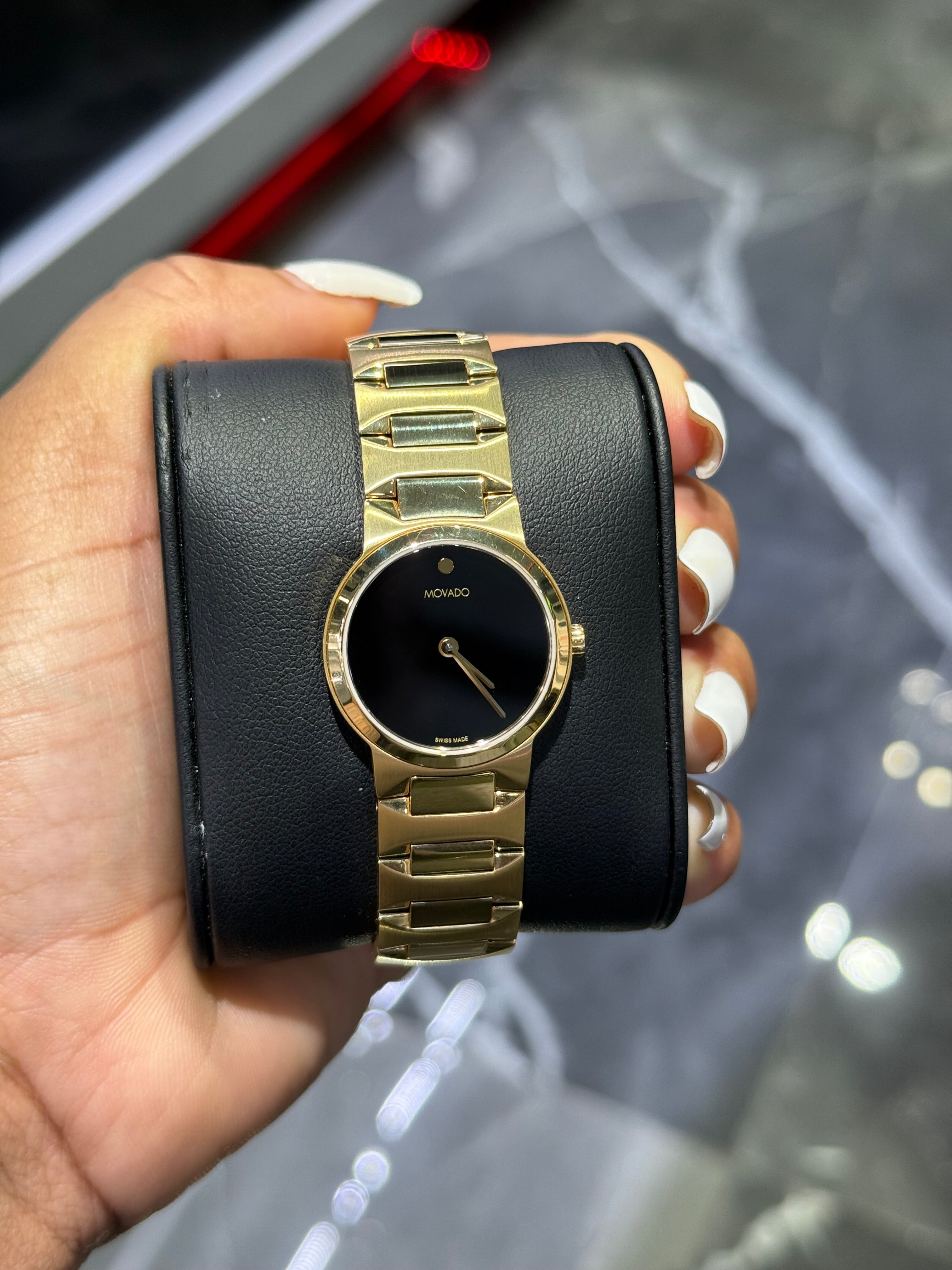 Gold wristwatch with black face held in a hand against a blurred background