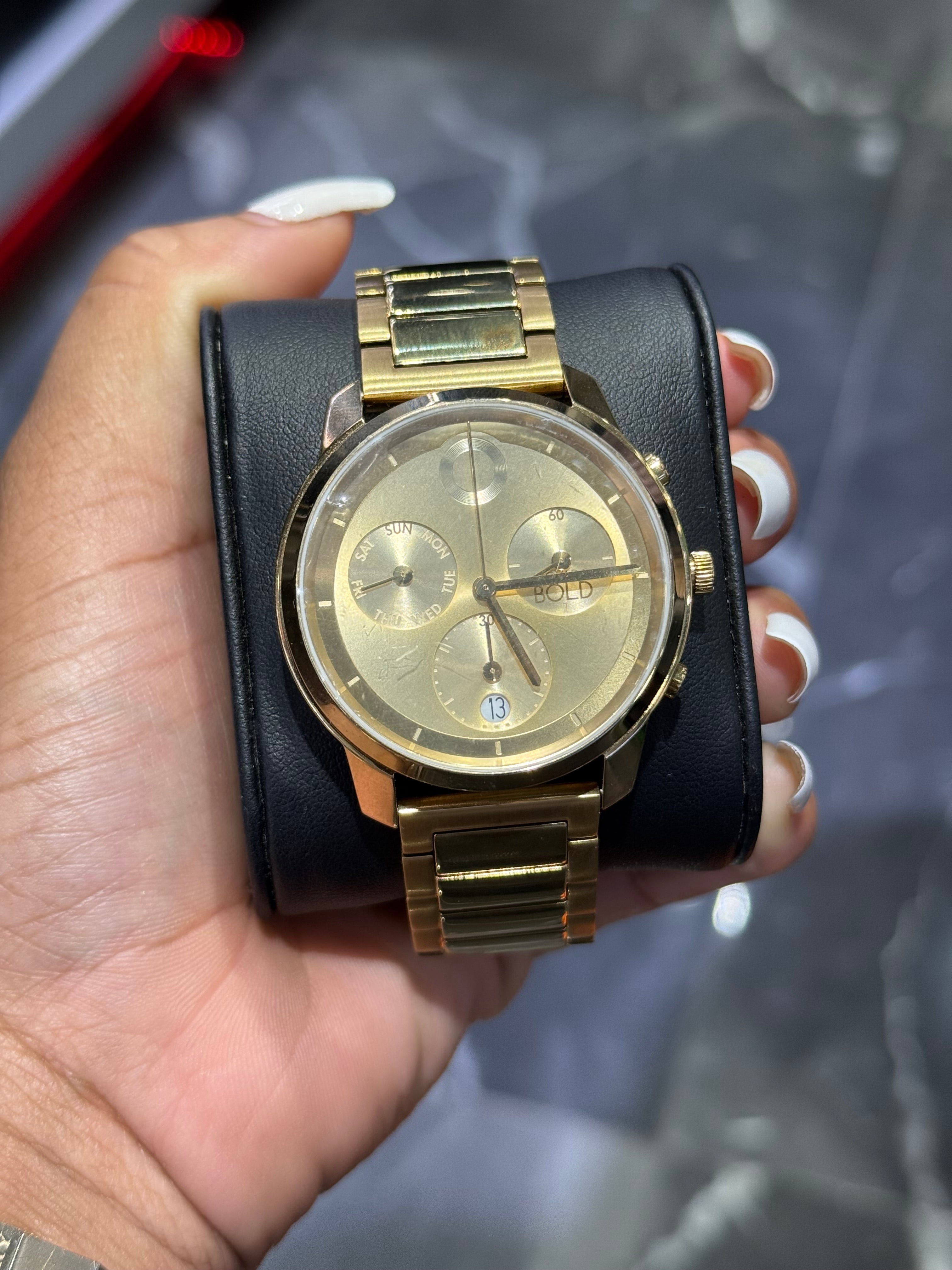 Gold watch with black leather strap held in a hand against a blurred background