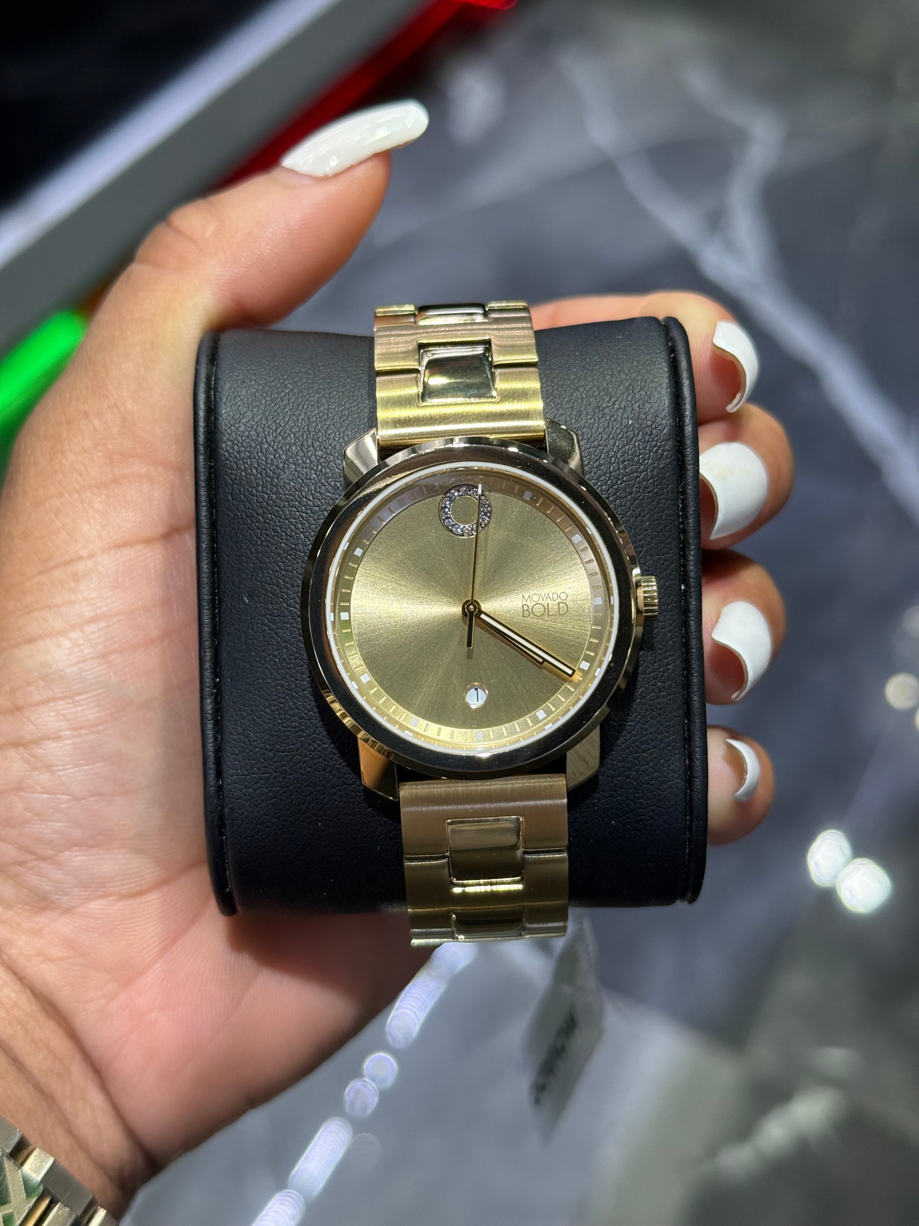 Gold watch with black leather strap held by a hand against a blurred background