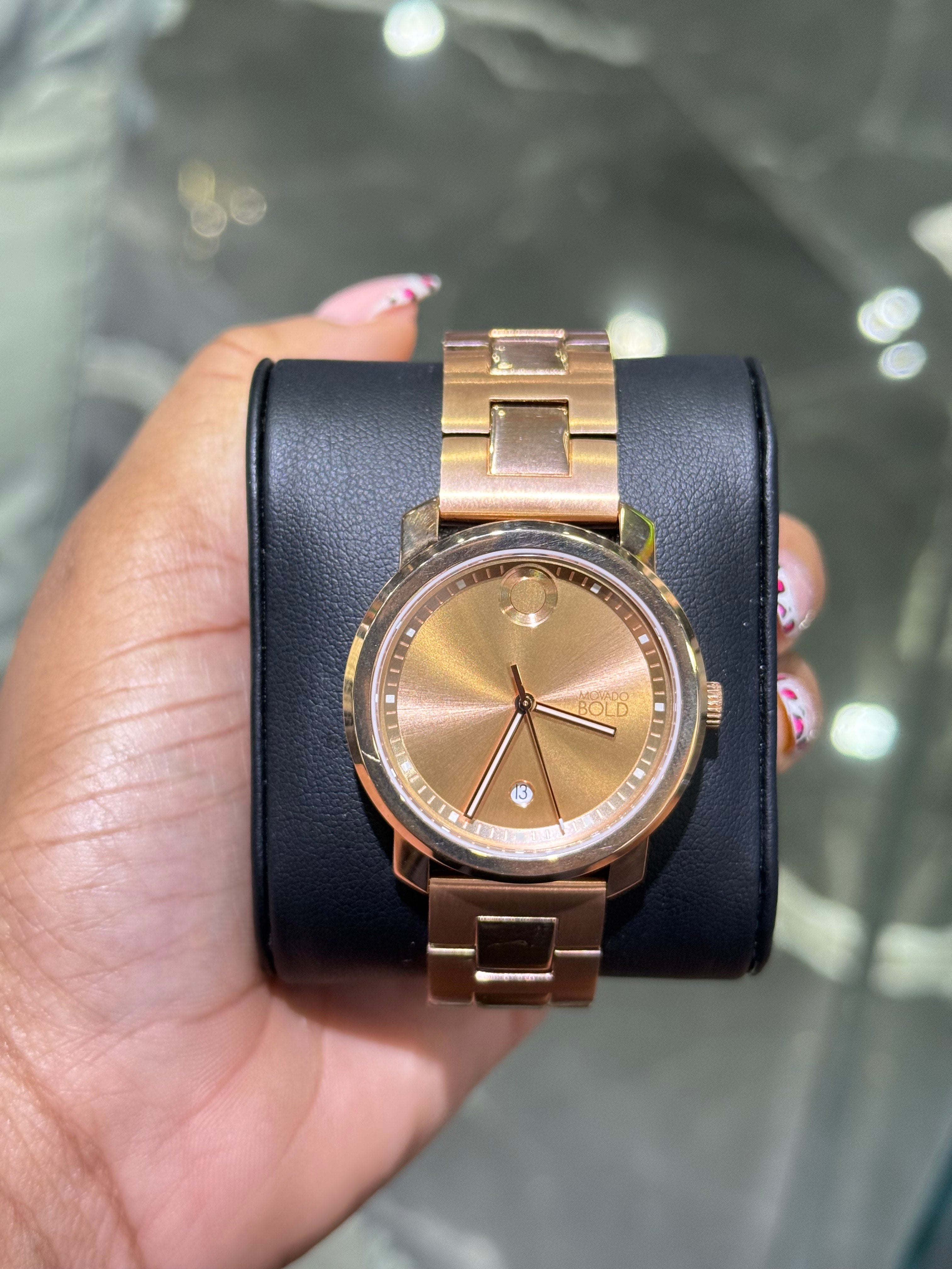 Gold watch with black leather strap held by a hand against a reflective surface.