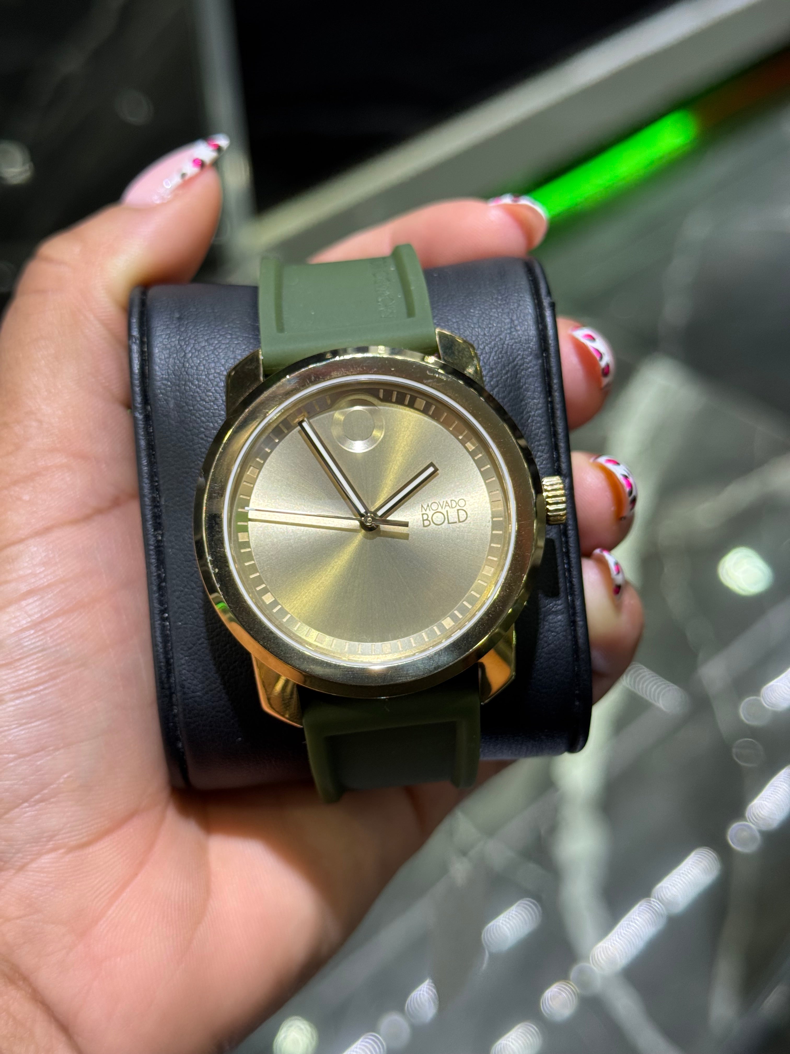 Gold watch with black strap held in a hand against a blurred background