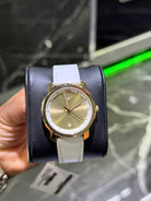 Gold watch with a white strap held by a hand against a blurred background