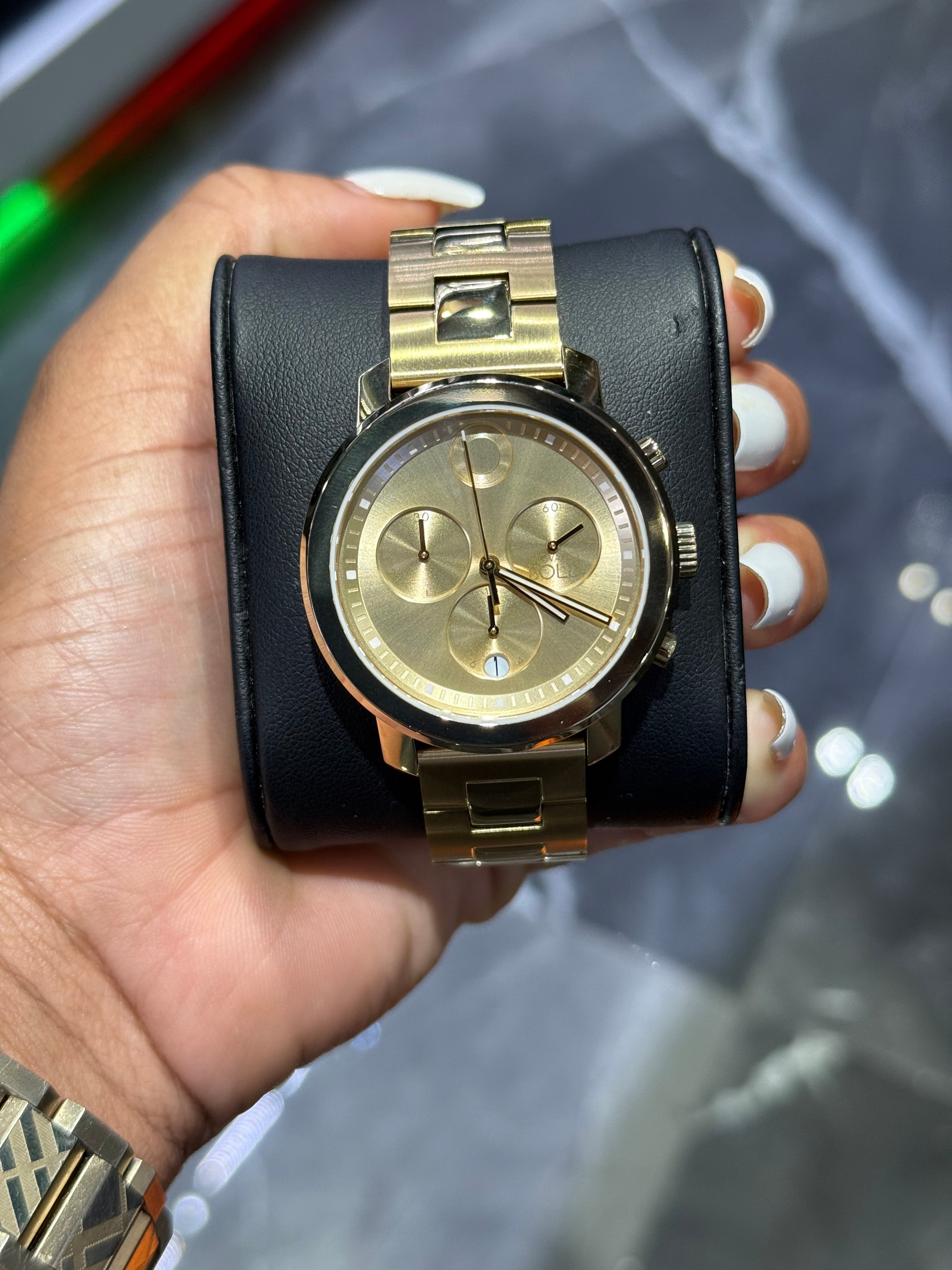 Gold wristwatch with black leather strap held in a hand against a reflective surface.
