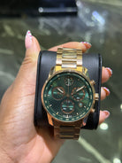 Gold and black wristwatch held by a hand with a blurred background