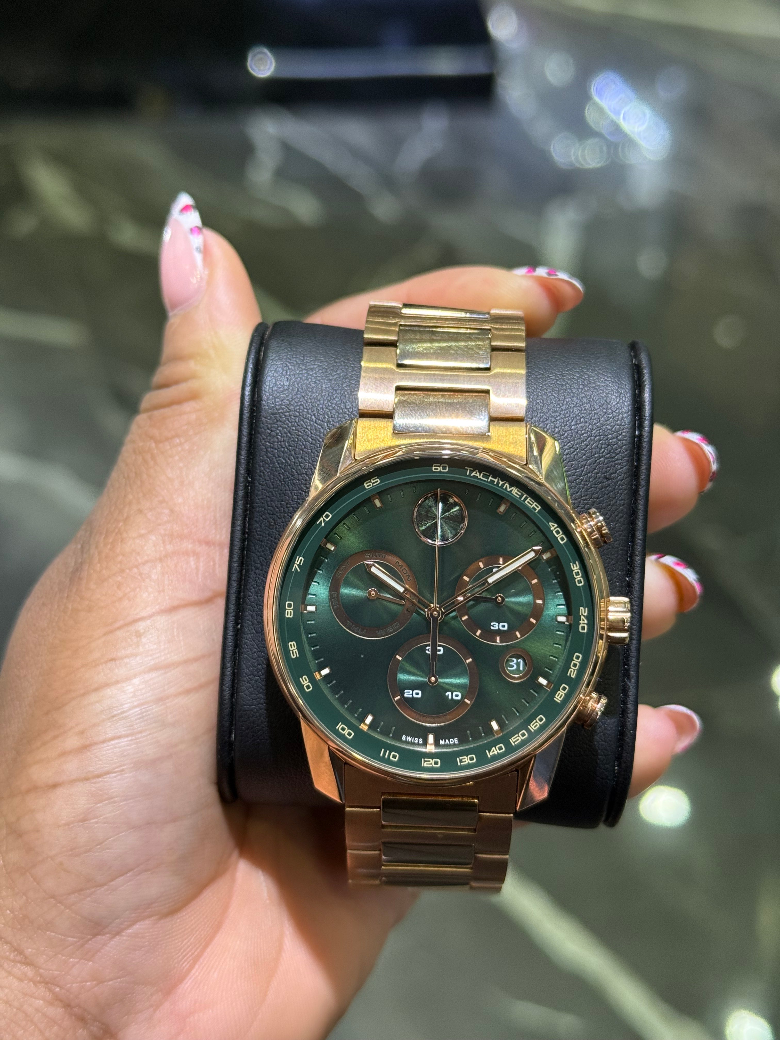 Gold and black wristwatch held by a hand with a blurred background