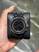 Black wristwatch with gold accents held in a hand against a neutral background