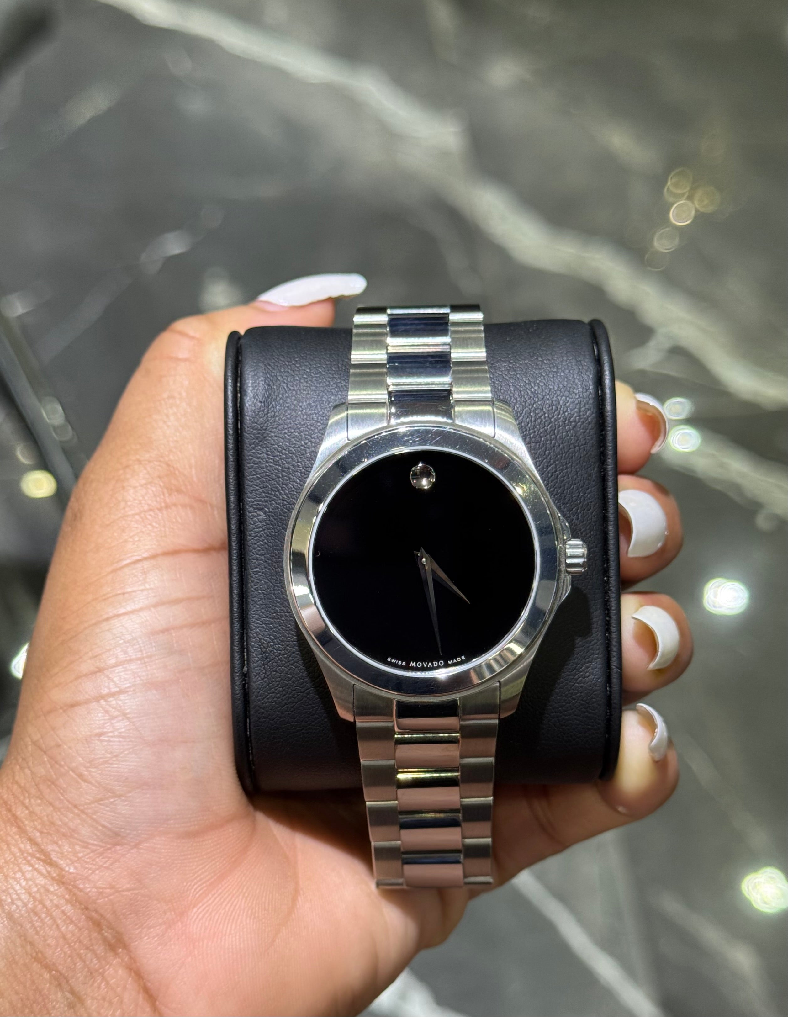 Silver watch with black face held in a hand against a marble background