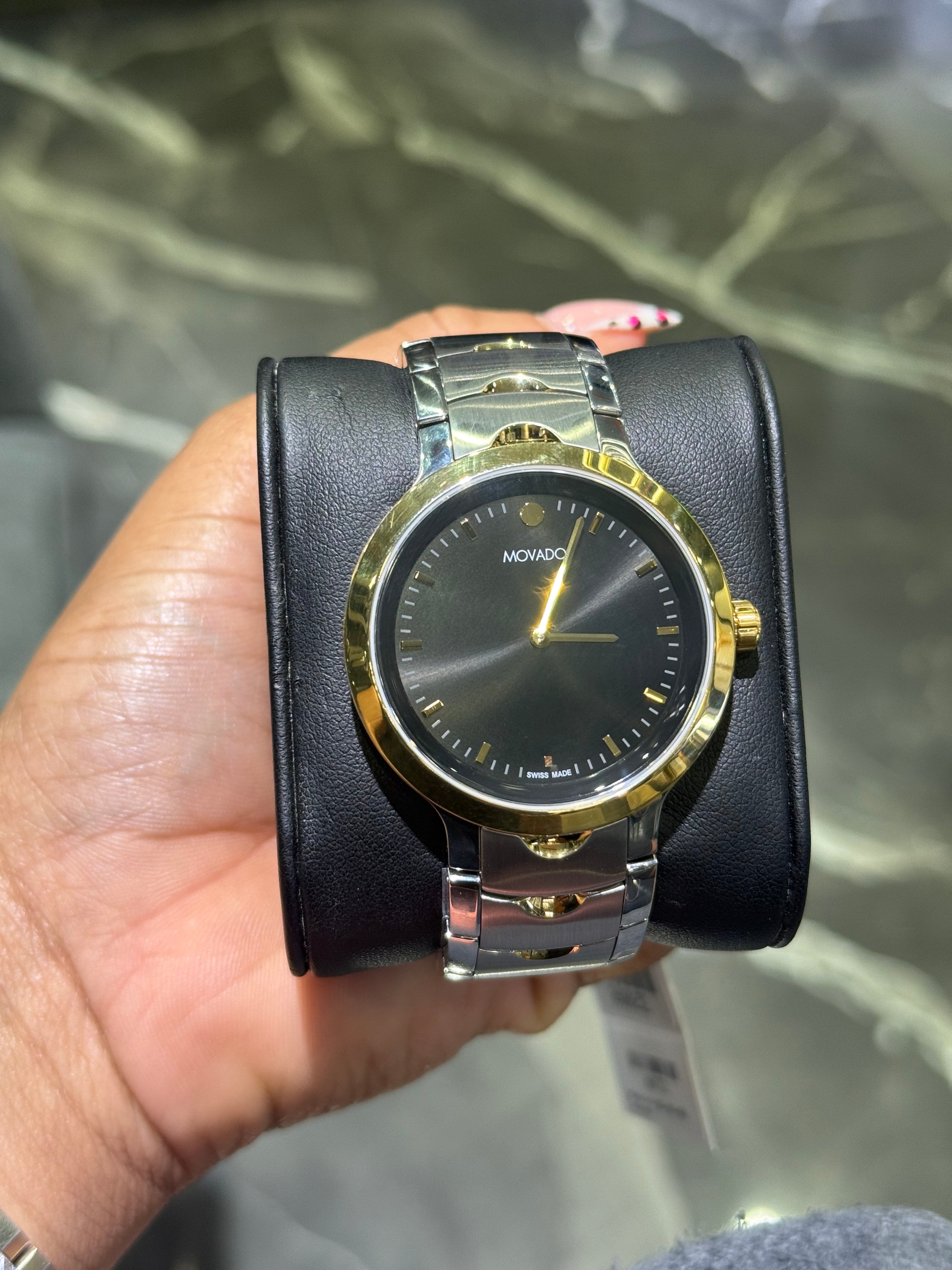 Gold and black watch held in a hand with a blurred background